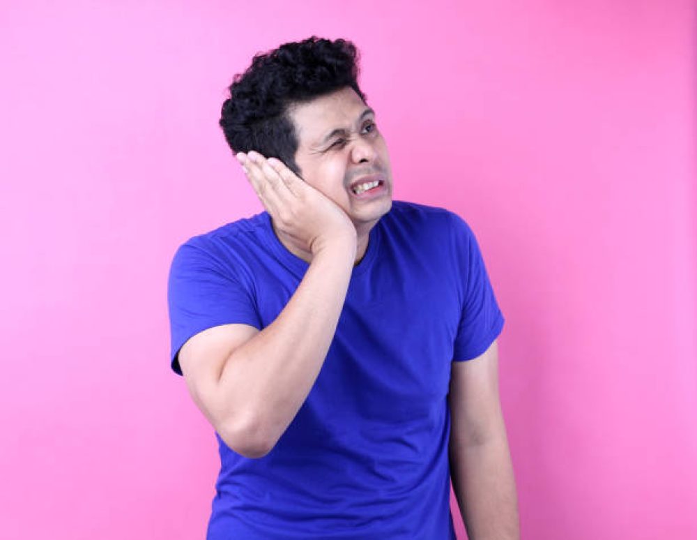 Portrait of Asian male having ear pain touching his painful head isolated on pink a background in studio.